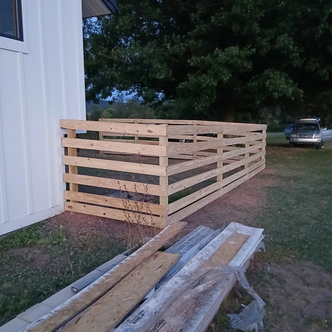 New wood railing frame built along the side of a white board-and-batten house
